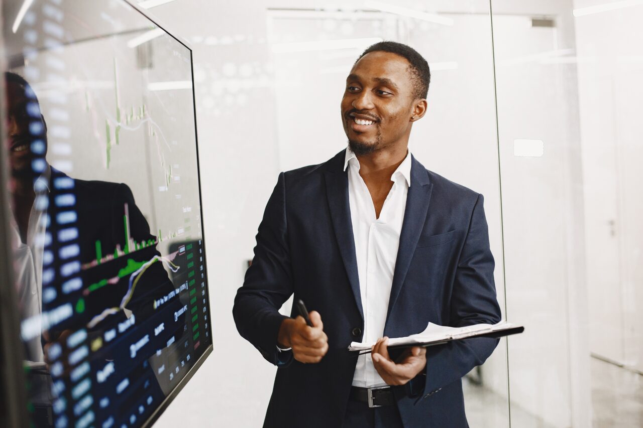 African man in a black suit. Big TV screen. Guy shows presentation.
